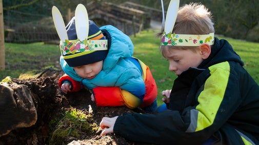 Two children wearing bunny ears looking closely at a fallen log